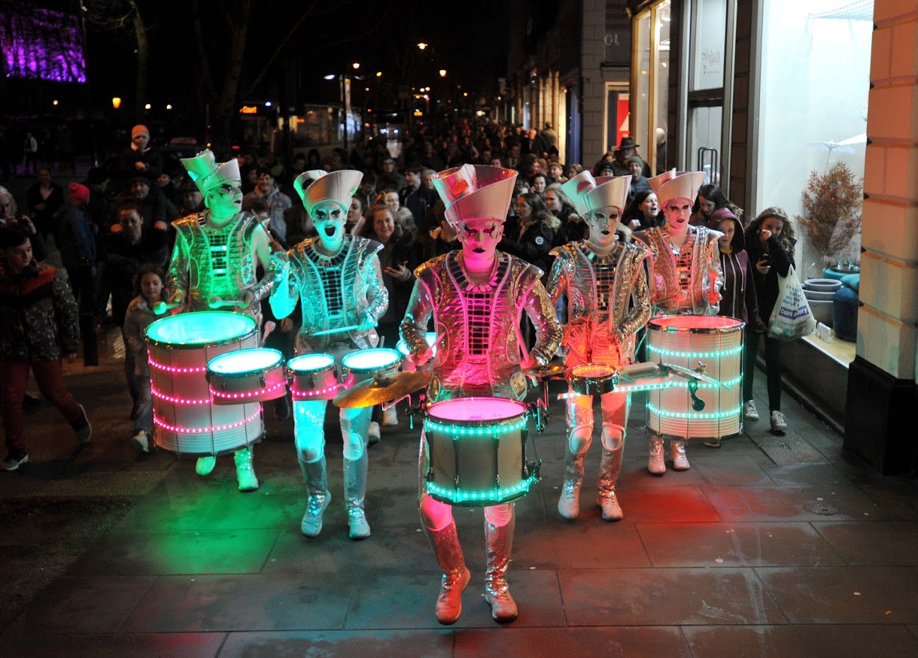 Spark! street performers lit up in different colours being watched by spectators