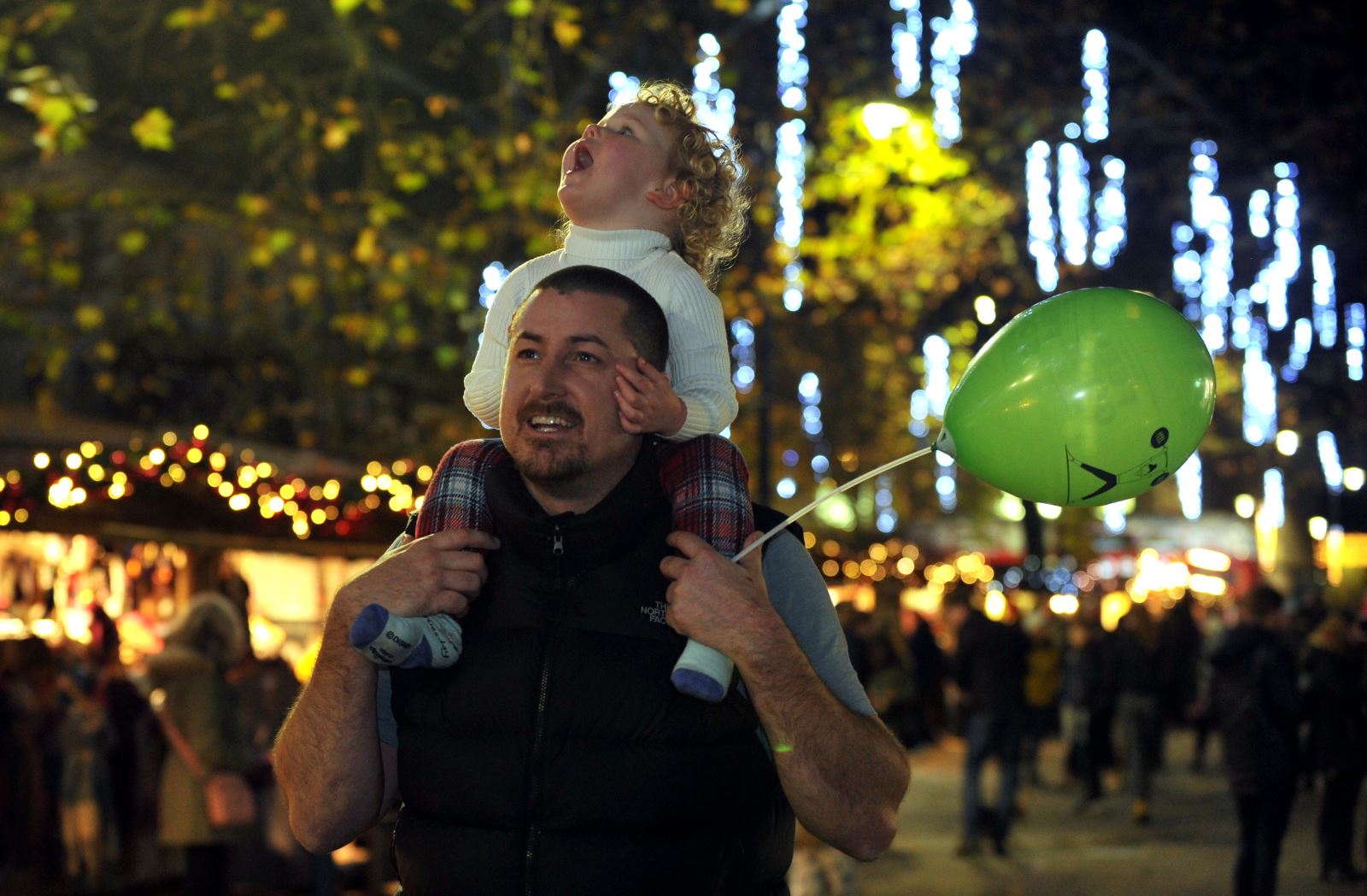 Child on father's shoulder enjoying Christmas lights