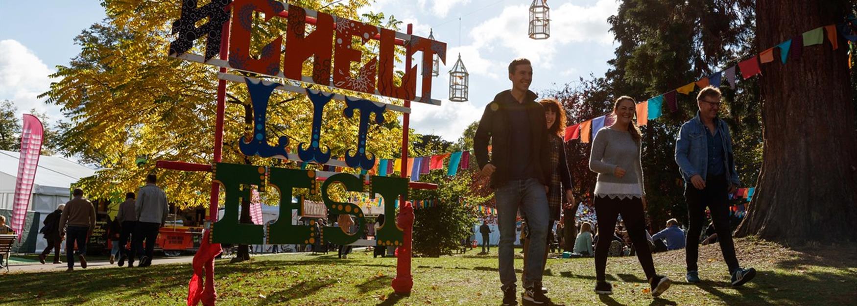 Group of people walking passed Cheltenham Lit Fest sign in Montpellier Gardens