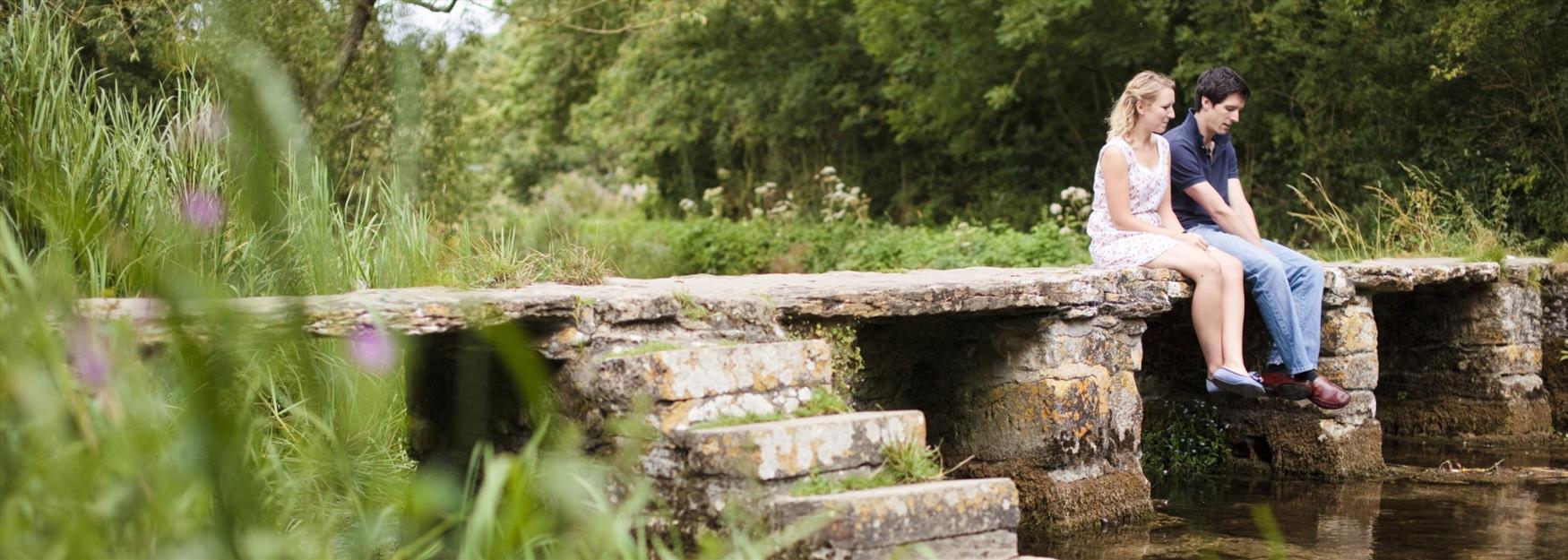 Couple sitting on a low bridge over a stream
