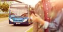Couple looking at mobile phone at a bus stop, with bus approaching